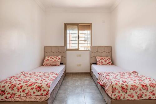 2 Betten in einem Zimmer mit weißen Wänden und einem Fenster in der Unterkunft Appartement en résidence (shahid,clim,wifi…) in Marrakesch
