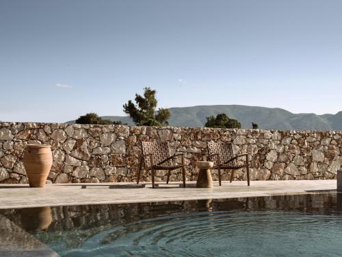 un muro di pietra con due sedie accanto alla piscina di Onore Villa, Featuring Heated Pool, By ThinkVilla a Gaïtánion
