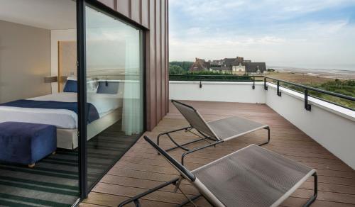 a bedroom with a bed and a chair on a balcony at Thalazur Cabourg - Hôtel & Spa in Cabourg