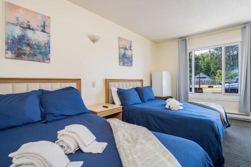 2 bedden in een slaapkamer met blauwe lakens en handdoeken bij Beach Club by Beach1 Motel in Wasaga Beach