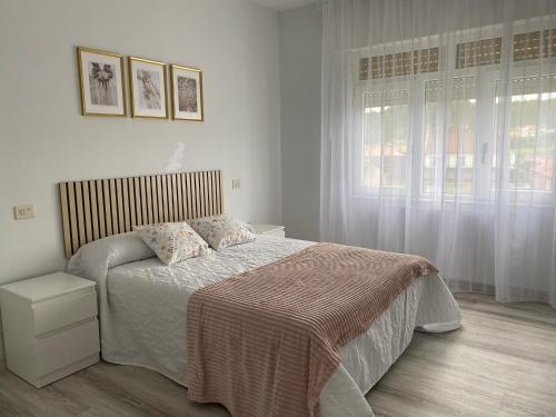 a white bedroom with a bed and a window at A Xaneiriña in Camariñas