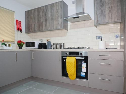 a kitchen with a stove with a yellow oven mit at Modern Spacious 4 Bed House-with Private Parking in Birmingham 
