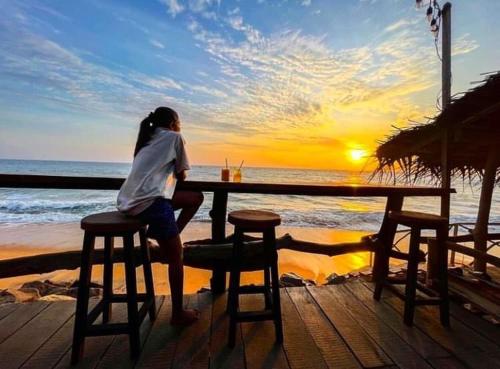 a woman sitting at a table on the beach with the sunset at Backpack Beach Hostel & Reggae Bar in Galle