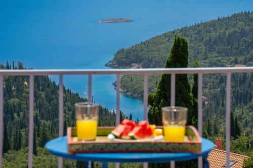 a table with two glasses of orange juice and fruit on a balcony at Villa Apollo up to 8px, private pool in Fiskardho