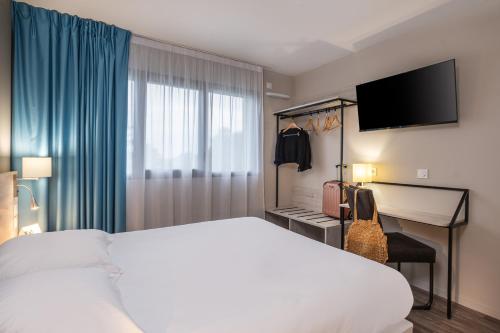a hotel room with a bed and a desk with a television at The Originals City, Relais d'Estillac, Agen Sud in Estillac