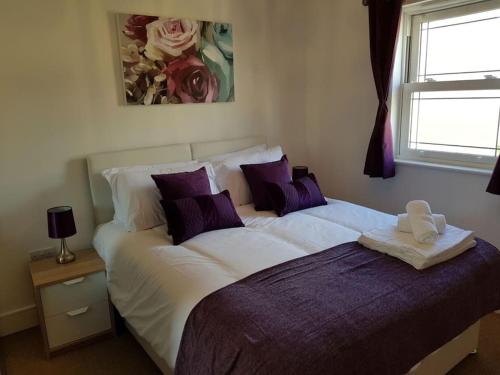 Guest Homes - Propelair Apartment في كولشستر: غرفة نوم مع سرير كبير مع وسائد أرجوانية