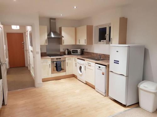 een keuken met witte apparatuur en houten vloeren bij Guest Homes - Propelair Apartment in Colchester