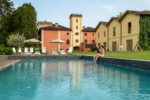 a woman sitting on a wall next to a swimming pool at Villa Clementina - Prosecco Country Hotel in San Pietro di Feletto