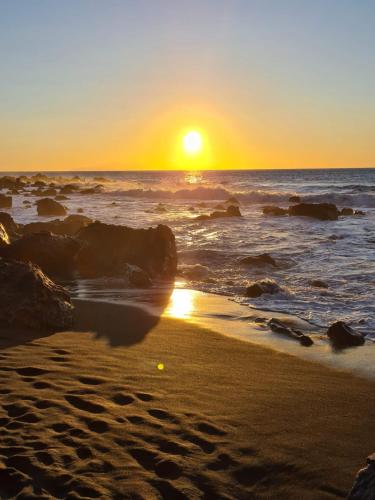 a sunset on a beach with the ocean and rocks at Mini Suite 35 qm in Calera