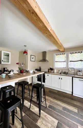 une grande cuisine avec des armoires blanches et des tabourets noirs dans l'établissement Le Clos de l'Angley Gîtes et Écurie, à Caffiers