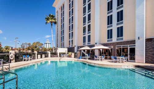 a swimming pool in front of a building with tables and chairs at Hampton Inn Orlando Near Universal Blv/International Dr in Orlando