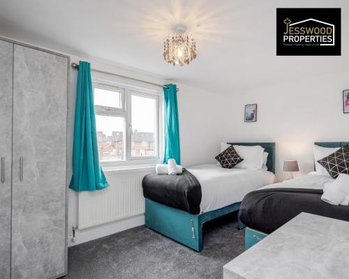 two beds in a room with blue curtains and a window at 6 Bedroom Contractor House at Jesswood Properties Short Lets With Parking,Wifi & Pool Table in Luton