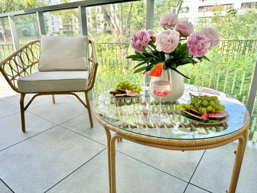 a glass table with a vase of pink flowers and a vase of fruit at ŻOLI STORK APARTMENTS - Hubnera 5 in Warsaw