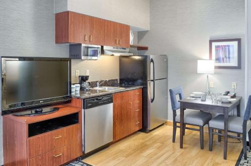 a kitchen with a television and a table with chairs at Homewood Suites by Hilton Mobile Airport-University Area in Mobile