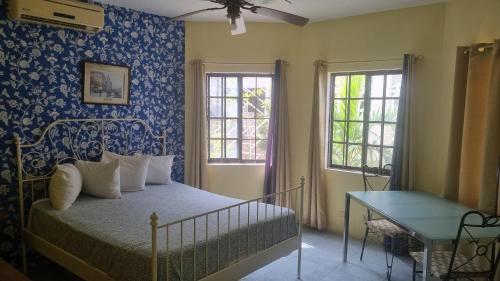 a bedroom with a bed and a table and two windows at Little Savoy Guest House new in Runaway Bay