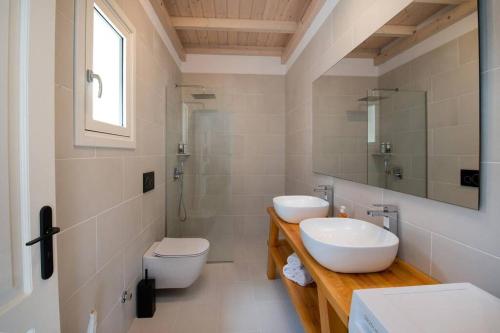 uma casa de banho com 2 lavatórios, um WC e um espelho. em Terra villa by PaxosRetreats em Lákka