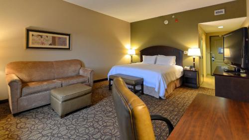 um quarto de hotel com uma cama, uma cadeira e um sofá em Hampton Inn Geneseo em Geneseo