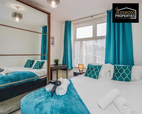 a bedroom with two beds with blue curtains and a mirror at Large 6 Bedroom Contractor House by Jesswood Properties Short Lets For Groups, Business And Leisure With Free Parking, Wifi and Pool Table in Luton