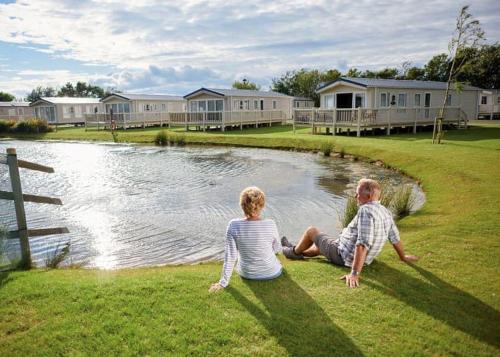 a man and woman sitting on the grass next to a pond at Blue Dolphin Holiday Park in Gristhorpe
