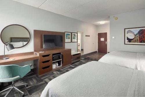 a hotel room with a bed and a desk with a mirror at Hampton Inn Louisville Northeast in Louisville