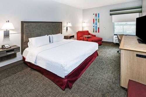 a hotel room with a large bed and a red chair at Hampton Inn Sulphur in Sulphur