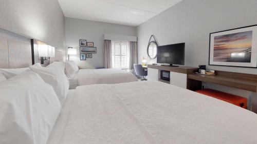 Habitación blanca con 2 camas y escritorio. en Hampton Inn St. Simons Island, en Saint Simons Island