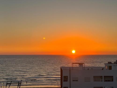 a sunset over the ocean with a building in the foreground at Oasis Mehdia vue sur mer in Kenitra