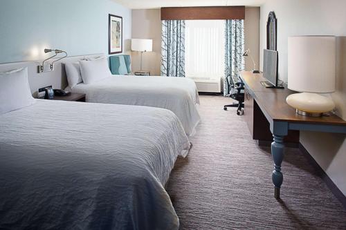 Habitación de hotel con 2 camas y escritorio con TV. en Hilton Garden Inn Albany Airport en Latham