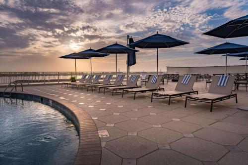eine Gruppe von Stühlen und Sonnenschirmen neben einem Pool in der Unterkunft Hilton Baton Rouge Capitol Center in Baton Rouge