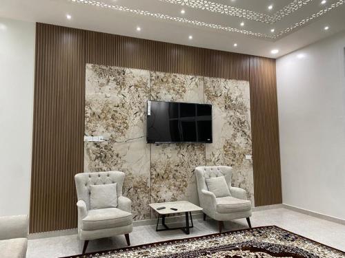 a living room with two chairs and a tv on a wall at Al Saad chalet in Al Ashkharah