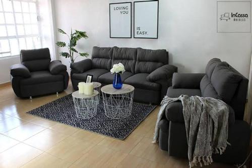 ein Wohnzimmer mit einem schwarzen Sofa und Stühlen in der Unterkunft Tu descanso in Mexiko-Stadt