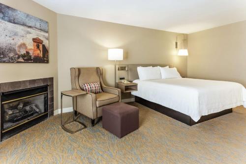 a hotel room with a bed and a chair and a fireplace at Hilton Garden Inn Saint Charles in Saint Charles