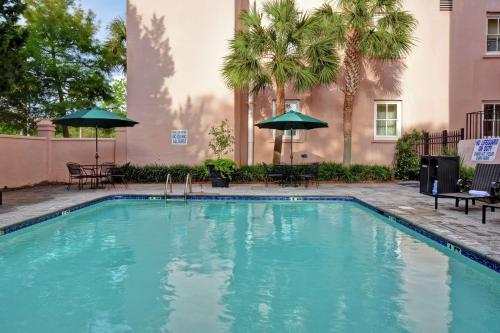 a swimming pool with chairs and umbrellas next to a building at Embassy Suites Charleston - Historic District in Charleston