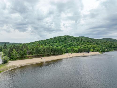 a body of water with a beach and a mountain at Les Lofts du Lac des Sables by Gestion ELITE in Sainte-Agathe-des-Monts