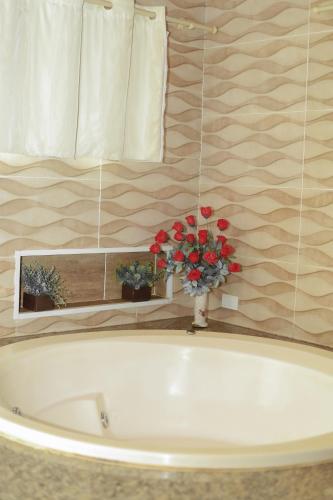 a bath tub with a vase with red flowers in it at Portal Da Mata in Santa Fé do Sul