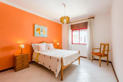 クアルテイラにあるApartamento T1 praiaのオレンジ色の壁のベッドルーム1室、ベッド1台、椅子1脚が備わります。