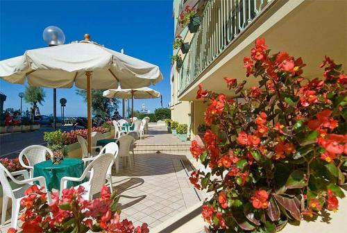 un patio con sillas, sombrilla y flores en Hotel Gloria, en Gabicce Mare