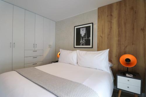 een slaapkamer met een bed met witte lakens en een oranje lamp bij Capac By Wynwood House in Lima