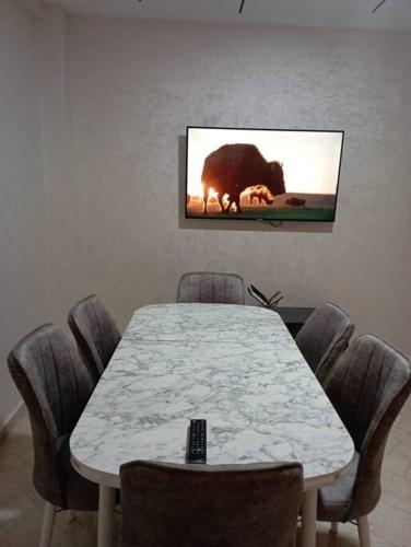 a white table with chairs and a tv on the wall at Eden Appartement avec Piscine Et Salle de Sport in El Jadida