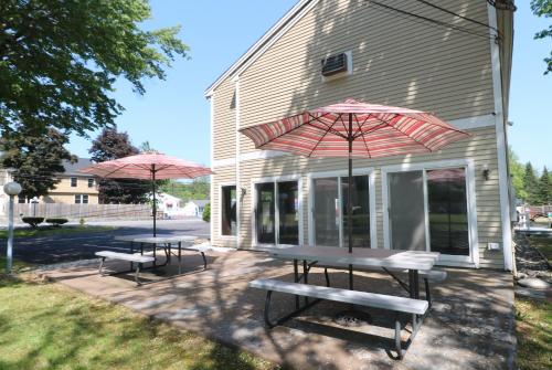 two picnic tables with umbrellas in front of a building at Classic Inn in Saco
