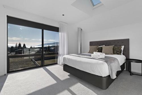 a white bedroom with a bed and a large window at Cardrona Creekside Apartment in Cardrona