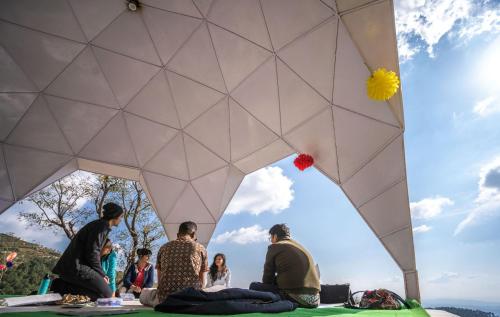 a group of people sitting on the ground under a umbrella at Hill Ventures Adventure Camp and Restaurant in Dharamshala