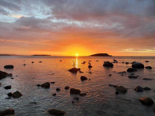 a sunset on a beach with rocks in the water at Seaview Getaway - 2 2 Solway Cres EncounterBay - BYO Linen in Encounter Bay