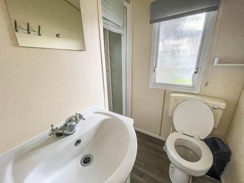 uma casa de banho com um lavatório, um WC e uma janela. em Lovely Caravan At Valley Farm Holiday Park, Sleeps 8 Ref 46127v em Great Clacton