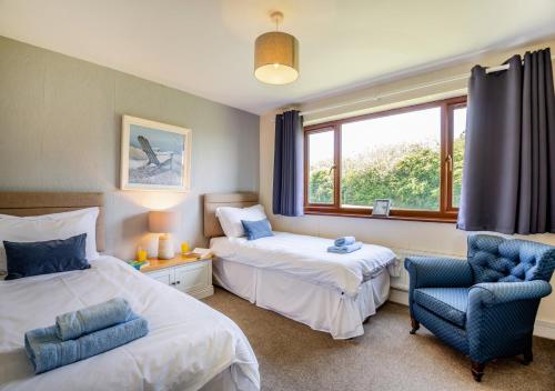 a bedroom with two beds and a chair and a window at Penmaen Bach in Pwllheli