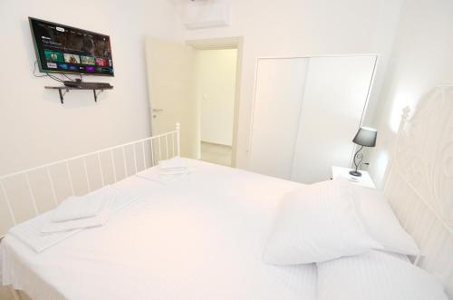 a white bedroom with a bed with a tv on the wall at Kjara Lux Apartment in Tivat