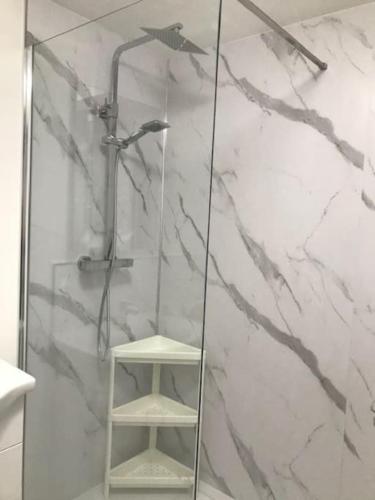 a shower with a glass door and a stool in a bathroom at Dolly Cottage Colchester in Mile End