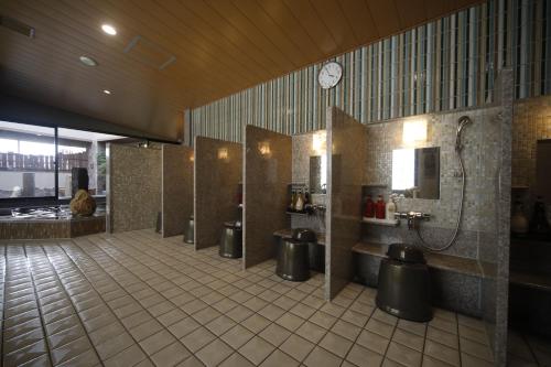 Dormy Inn Oita في أويتا: حمام عام فيه أكشاك وساعة على الحائط