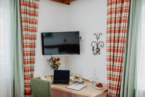 a desk with a laptop and a tv on a wall at Weßner Hof Landhotel & Restaurant in Marquartstein
