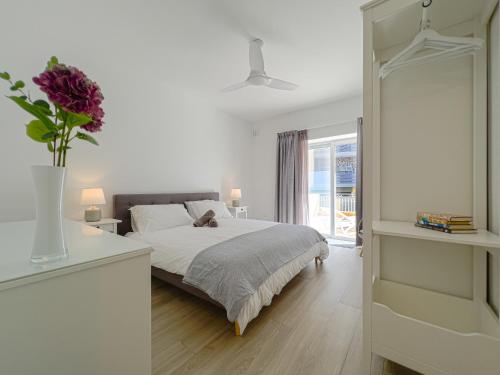 a white bedroom with a bed and a vase with flowers at 21 Townhouse in St Julians in Paceville